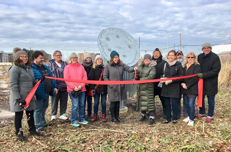 Roughly a dozen people standing in front of the Nesewin sculpture for a ribbon cutting ceremony