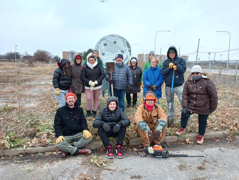 A group of thirteen volunteers in front of the Nesewin sculpture, after a working session